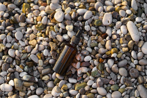 Fototapeta Brown jar of serum with dispenser on pebbles by the sea on the beach. Natural cosmetics with extract and oils, skin care and restoration, reduction of wrinkles and age-related changes.