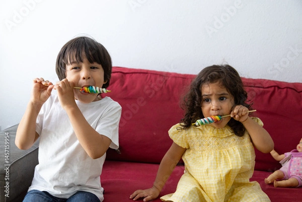 Obraz Siblings enjoying colorful lollipops on a couch