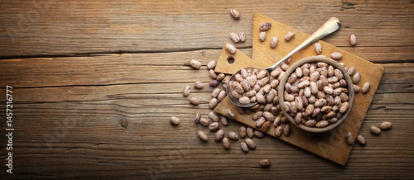 Fototapeta Dried pinto beans in wooden bowl with cutting board and spoon on old wooden background, close-up, space for text.