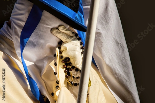 Fototapeta TARANTO, ITALY - APRIL 13-14, 2017: On Holy week members of the fraternities in white robes, covering their faces with hoods, follow an ancient route carrying the statues of the Stations of the Cross