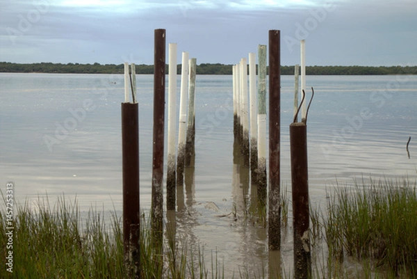 Obraz Posts standing on the shore of Cananeia channel early morning at sunrise. Calm waters, clear sky, sunny day