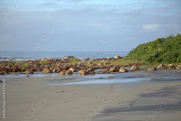 Obraz Itacuruca beach, Cananeia, south Sao Paulo state, rocks spread out on beach sand, green vegtaion, clear blue sky, sunny day morning