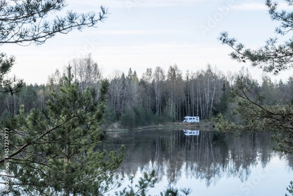 Fototapeta Matsimae, Estonia - May 04 2025: Camper Car parking on the shore of Vahesaare Lake near Seli Bog. Reflections of trees and Blue Sky on Still Water on a Bright Spring Day in Protected Wetland Landscape