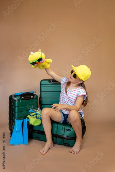 Fototapeta Cheerful child in yellow glasses and hat with toy duckling sits on green suitcases with flippers and diving mask. Family on vacation. Sea travel concept.