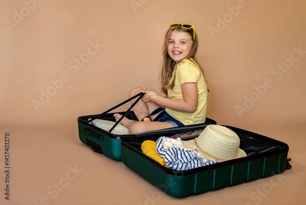 Fototapeta Happy child sitting in open green suitcase, excited about summer vacation and ready for vacation on beige background with space for text. Vacation, journey, flight. Travel concept.