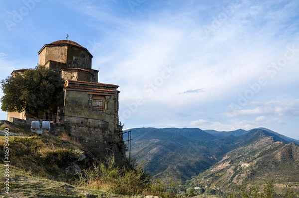 Fototapeta Jvari Monastery, a historic Georgian Orthodox monastery, sits atop a cliff overlooking a mountainous landscape under a partly cloudy sky