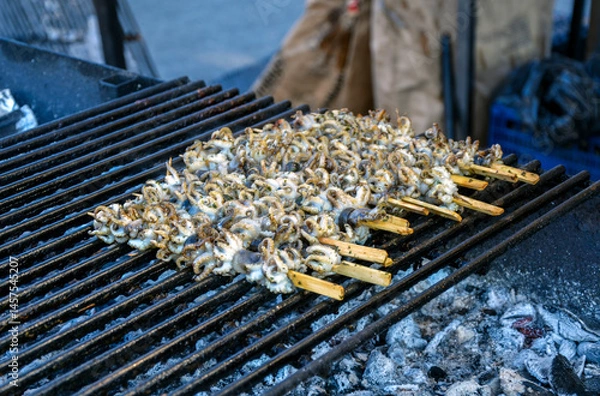 Fototapeta Fresh octopus skewers being grilled over open charcoal flames, showcasing a popular street food delicacy