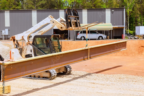 Obraz Construction worker operates forklift skid steer loader, moving large steel beam at building site