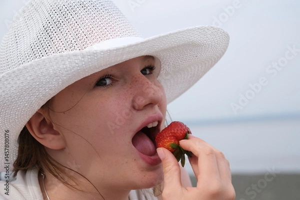 Obraz Girl eating strawberries smiling happy looking to the side on sea background with copy space. Beautiful young mixed race Asian and Caucasian woman eating healthy. High quality photo