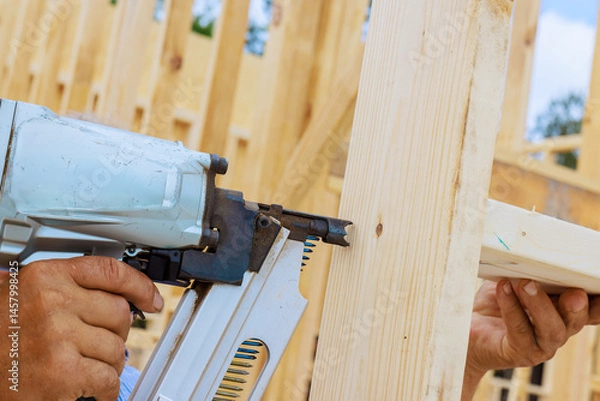 Obraz Craftsman during teamwork nail gun to fasten wooden beam at construction site