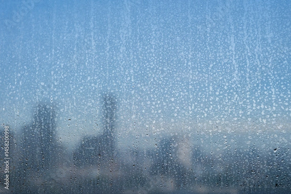 Fototapeta Raindrops on a glass window with a blurry cityscape in the morning background.