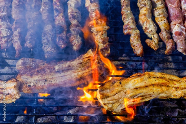 Fototapeta A grill filled with skewers and pork belly of meat cooking over open flames.