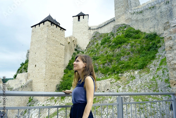 Fototapeta Tour of the famous Golubac Fortress: portrait of a smiling woman standing against the backdrop of defensive walls and high medieval towers. Traveling around Serbia: visit to the Đerdap National Park.
