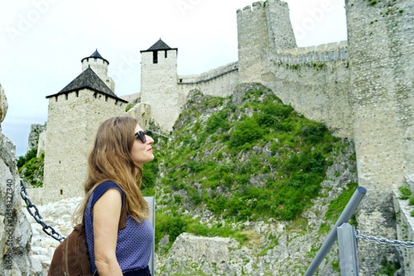 Fototapeta The most interesting places in Serbia - a tour of the Golubac fortress: a woman on a tower number 8. A smiling female tourist with a backpack examines the architecture of the ancient fortification.