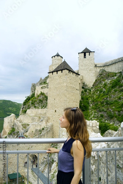 Fototapeta Visiting the most scenic places in Serbia: portrait of a woman standing at the viewpoint of the Golubac fortress. A female tourist against the background of the towers of a medieval European castle