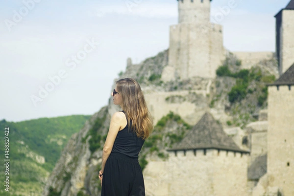 Fototapeta Vacation in Europe: a female tourist enjoys the view while standing in front of an ancient castle. Must see attractions in Serbia: a woman near of the Golubac Fortress in the Derdap National Park