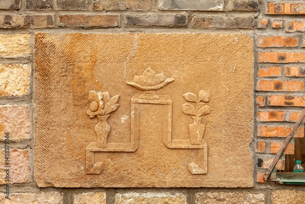 Fototapeta An ancient bas-relief depicting various flowers is mounted into a brick wall
