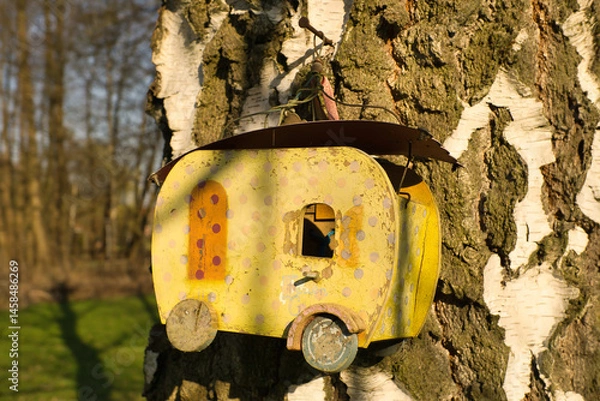 Fototapeta A yellow birdhouse in the shape of a caravan, attached to a tree trunk