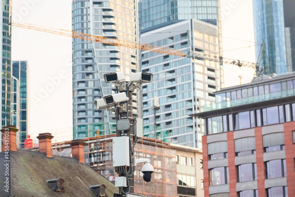 Obraz Street pole with CCTV cameras against the backdrop of skyscrapers.