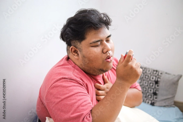 Obraz Unhealthy Asian Obese Man Using Inhaler and Touching His Chest While Sitting on Bed
