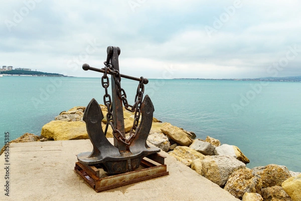 Obraz Rustic anchor stands on stone platform by the Black sea, with calm blue waters and cloudy sky creating peaceful coastal scene in Gelendzhik