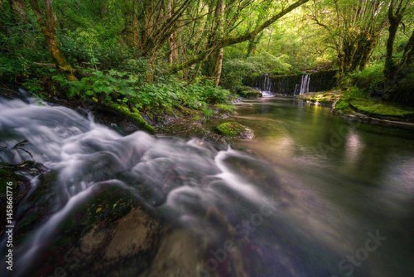 Fototapeta A small stream flows into a wide pool under a dam