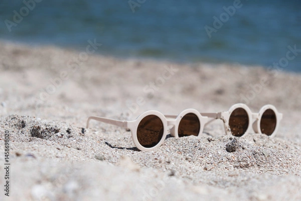 Obraz Two pairs of white round sunglasses that are lying on the beach. Blue sea and sun-protected crepe, warm weather, vacations, travel.High quality photo