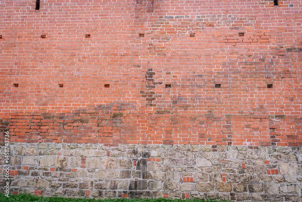 Obraz Weathered red brick and stone wall with aged textures, visible damage, and grassy base, suitable for backgrounds or architectural detail..