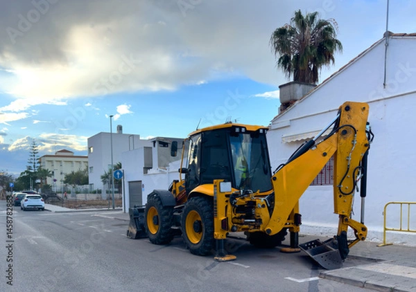 Obraz Tractor with bucket at road works in a Spanish city. Street renovation in Spain. Yellow construction tractor with bucket at construction works.