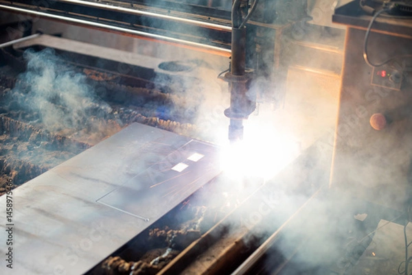 Fototapeta Plasma cutting process in metal fabrication workshop with smoke and sparks during operation