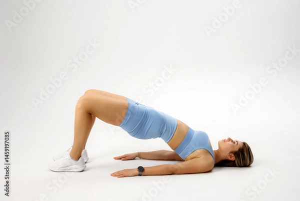 Fototapeta Woman practicing glute bridge exercise on a white background for fitness and strength training