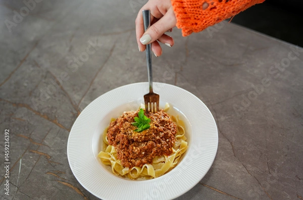 Fototapeta Close up view of eating pasta with tomato sauce, and parsley with a fork.