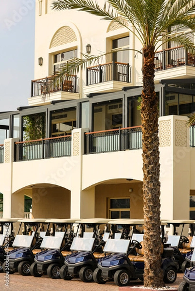 Obraz Luxury Golf Resort with Line of Golf Carts and Palm Trees Elegant golf resort exterior featuring a row of modern golf carts parked