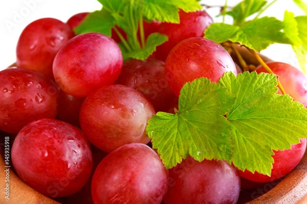 Fototapeta Bunch of fresh red grapes and leaves in a wooden plate on a light background