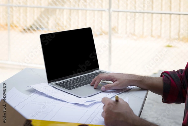 Obraz Male architect working with laptop on blueprint architects project in outdoor office.