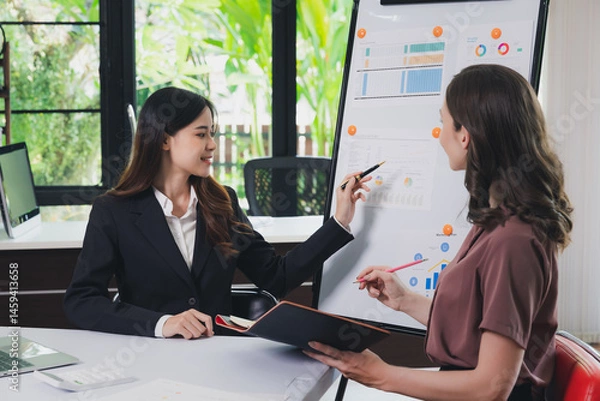Obraz Businesswoman making a presentation at work in front of colleague. Businesswoman coach mentor explain graph chart on flipchart corporate group workshop training in meeting room.