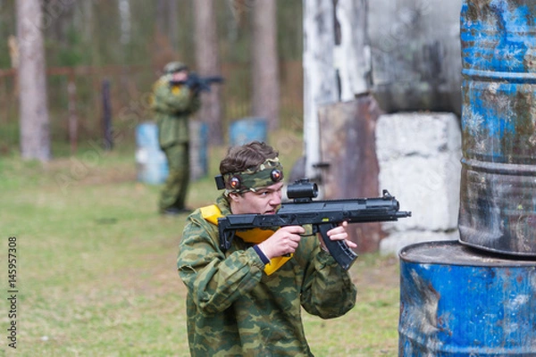 Obraz Paintball sportsman in ambush behind rusty barrels