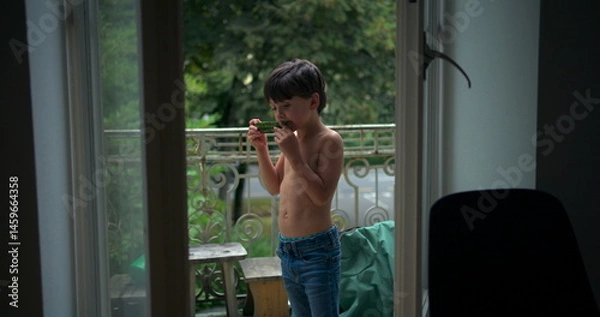 Fototapeta Boy enjoying a slice of watermelon while standing on a balcony, savoring a refreshing snack in a relaxed outdoor environment, surrounded by greenery