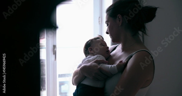 Fototapeta Mother holding her baby tenderly while standing near a window, sharing a quiet moment of connection in the soft natural light at home