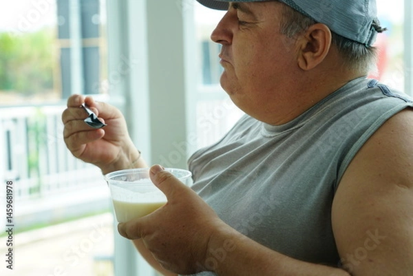 Obraz Fat Caucasian senior man with potbelly after workout hungry eating breakfast yoghurt,fruit salad healthy food and weight loss in fitness club. Health and wellness concept.