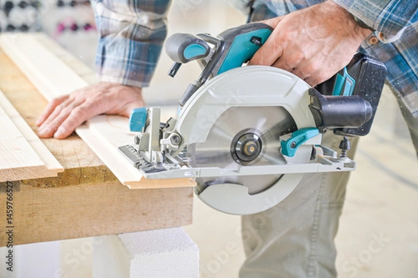 Fototapeta A skilled craftsman operates a circular saw on a wooden plank, showcasing precision and craftsmanship in a well-lit workshop environment, highlighting woodworking techniques