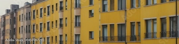 Fototapeta A yellow apartment building stands out among a row of similar structures , city photography, yellow