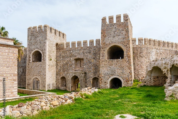 Fototapeta Historic stone castle wall featuring intricate architecture, vintage arched entryways, and a vibrant green lawn with clear skies, ideal for history and architecture enthusiasts...