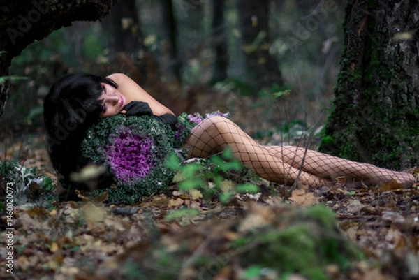 Fototapeta Slender brunette beauty in the image of a forest fairy lies on the ground. Decorative cabbage instead of a bouquet. Artistic creative photography.