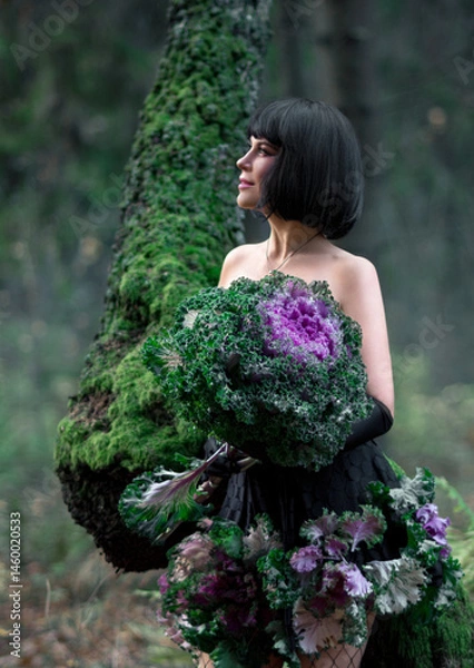 Fototapeta Portrait of a young brunette woman in a creative image. A large head of decorative cabbage and a hat made of cabbage leaves. Art photography.