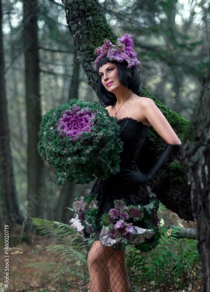 Fototapeta Portrait of a young brunette woman in a creative image. A large head of decorative cabbage and a hat made of cabbage leaves. Art photography.