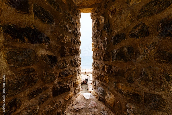 Fototapeta Narrow View Through an Ancient Stone Wall Corridor to the Sea Beyond..
