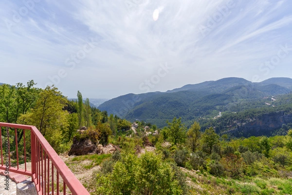 Fototapeta Elevated garden area with greenery, a red rail fence, and stunning views of distant blue mountains under a bright clear sky...