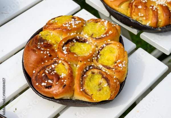 Obraz Freshly baked cinnamon rolls filled with sweet yellow cream and topped with sugar sit invitingly on a rustic wooden table, surrounded by a warm, inviting atmosphere