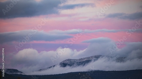 Obraz Snow-dusted mountains surrounded in clouds at sunset